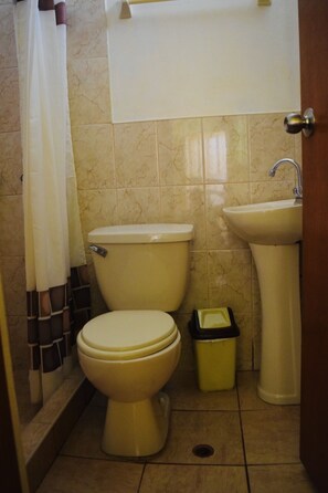 A small bathroom with a toilet, sink, and trash bin.