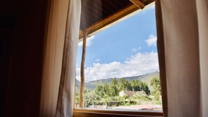 Una ventana con vistas a un paisaje montañoso, una estructura de madera y cielo despejado.