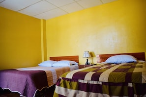 A hotel room with two beds, a nightstand with a lamp, and yellow walls.