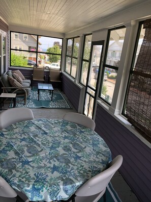 Relax in this inviting sunroom with a sofa, chairs, and a round table, offering a view of the street through the window with blinds.