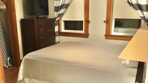 Un dormitorio con cama, cómoda, televisor y ventana con cortinas.
