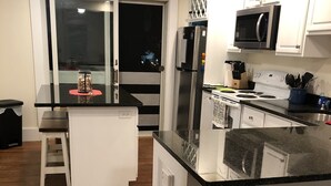 Una cocina compacta con armarios blancos, una encimera negra y un refrigerador de acero inoxidable.