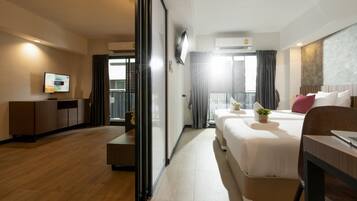 Een hotelkamer met een bed, bureau, televisie en een balkon met gordijnen.