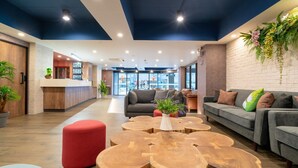 A modern lounge area with a reception desk, sofas, and a coffee table with a plant. - The Home Hotel (Bangkok)