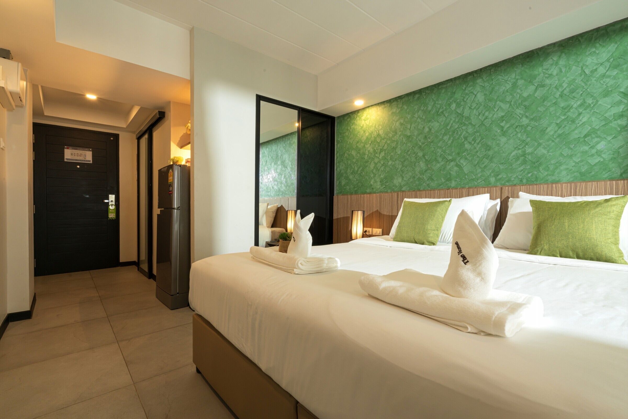 Quarto de hotel com uma cama grande, parede verde com textura e um espelho.