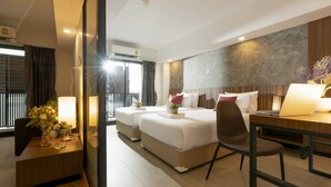 A hotel room with a large bed, a desk, and a chair. There is a window with curtains and a view of the outside. - The Home Hotel (Bangkok)