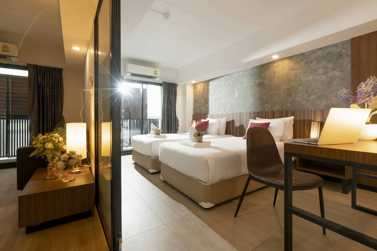 A hotel room with a large bed, a desk, and a chair. There is a window with curtains and a view of the outside.