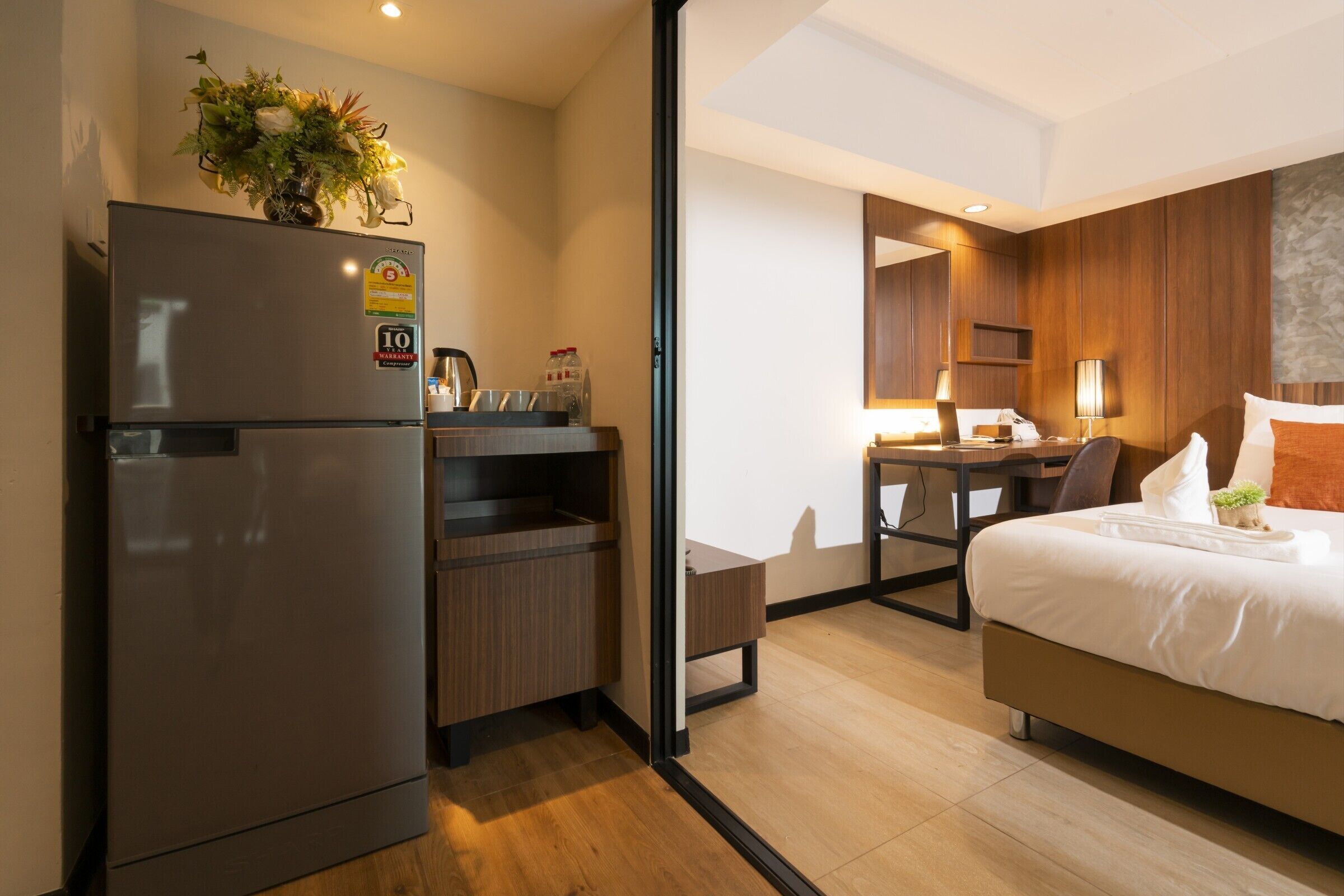 Una habitación de hotel moderna con refrigerador, una pequeña kitchenette, una cama y un escritorio.