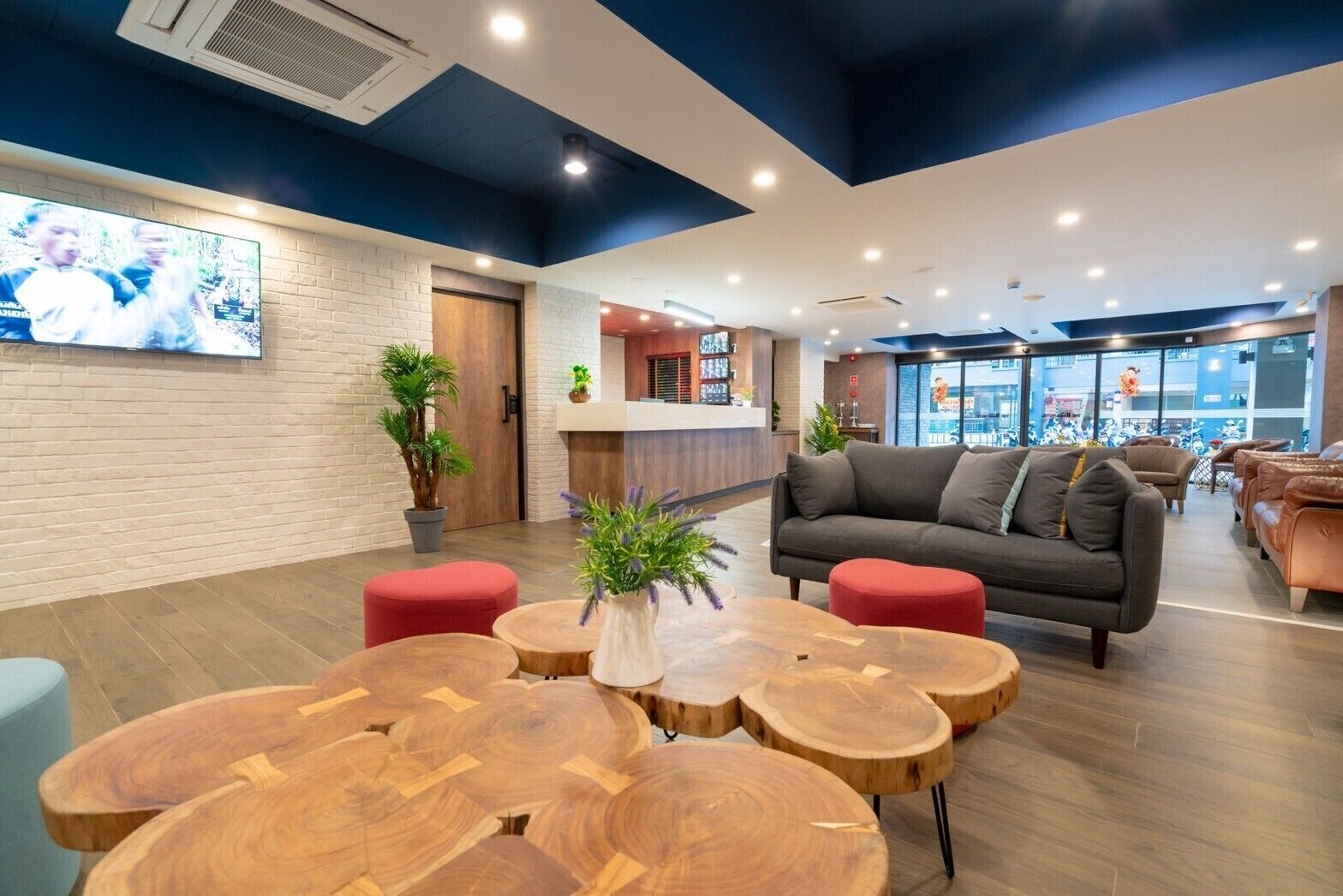 A modern lobby with a grey sofa, red ottomans, and wooden tables.