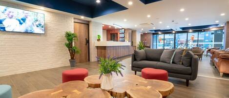 A modern lobby with a grey sofa, red ottomans, and wooden tables.