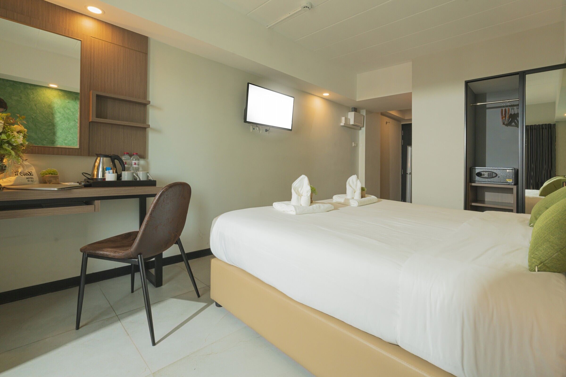 A hotel room with a bed, a desk with a chair, a TV, and a mirror.