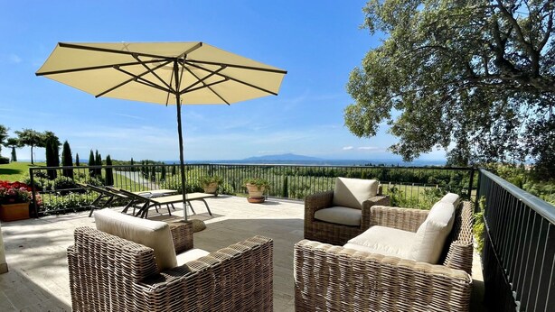 Eine Terrasse im Freien mit Korbmöbeln, einem großen Sonnenschirm und schöner Aussicht.