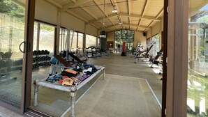 Ein großzügiger Fitnessraum mit unterschiedlichen Trainingsgeräten, großen Fenstern und einer Holzbalkendecke.
