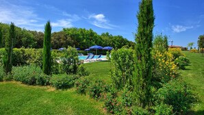 Ein Poolbereich mit blauen Sonnenschirmen, umgeben von üppiger Vegetation und blauem Himmel.