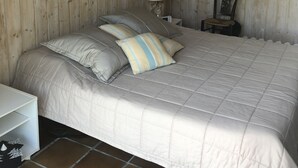 Ein Schlafzimmer mit einer holzverkleideten Wand, einem Bett mit gesteppter Bettdecke, zwei Kissen, einem Nachttisch mit Lampe und einem gerahmten Bild an der Wand.