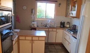 A compact kitchen with a stove, microwave, and sink. There is a window above the sink, and cabinets are present.