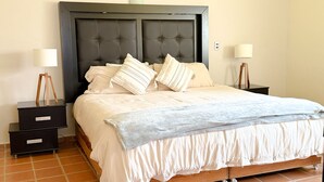 A neatly made bed with a tufted headboard, two bedside tables with lamps, and a tiled floor. - NICE HOUSE ONLY 5 STREETS FROM THE CITY CENTER (Col Centro Cuatilulco)