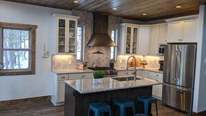 A modern kitchen with white cabinets, a stainless steel refrigerator, and a granite countertop. - Whispering Pines - LUXURY Cabin-Hot Tub, Fireplace, Huge Deck, Pool Tbl, 6 Acres (Florissant)