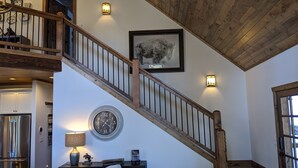 A staircase with wooden railings leading to a second floor, a clock, and a framed picture on the wall. - Whispering Pines - LUXURY Cabin-Hot Tub, Fireplace, Huge Deck, Pool Tbl, 6 Acres (Florissant)