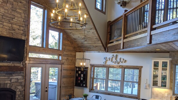 A spacious living area with a fireplace, a chandelier, a dining table with chairs, and a staircase leading to an upper level. - Whispering Pines - LUXURY Cabin-Hot Tub, Fireplace, Huge Deck, Pool Tbl, 6 Acres (Florissant)
