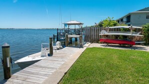 A wooden dock extending into calm water, a covered boat house, and a grassy area with a red boat. - Best Value on Manasota Key and Steps to Lemon Bay (Englewood)