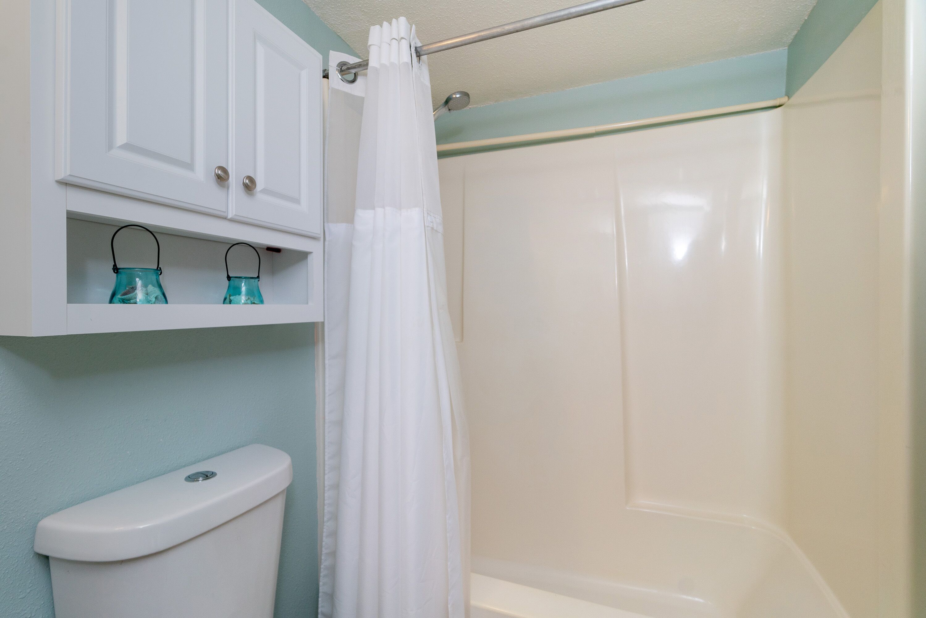 A bathroom with a toilet, a shower, and a shelf with two glass bottles.