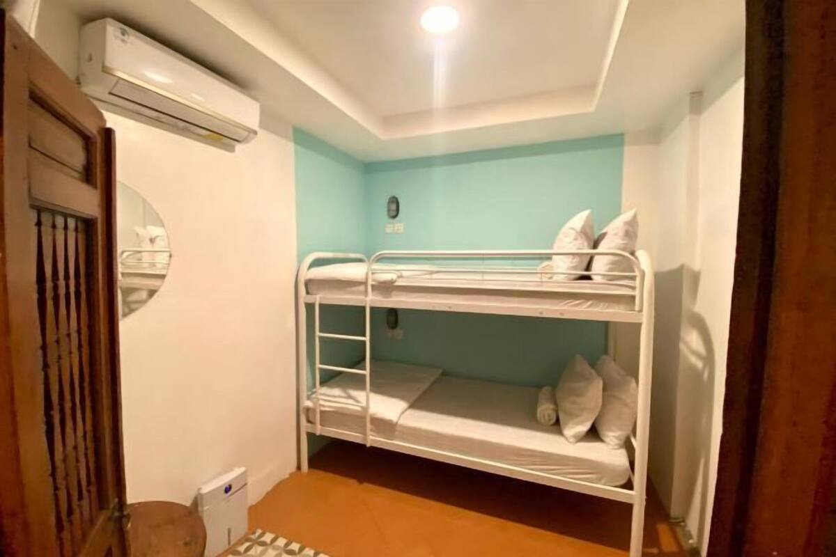 A bunk bed room with a ceiling fan, an air conditioning unit, and a small window.