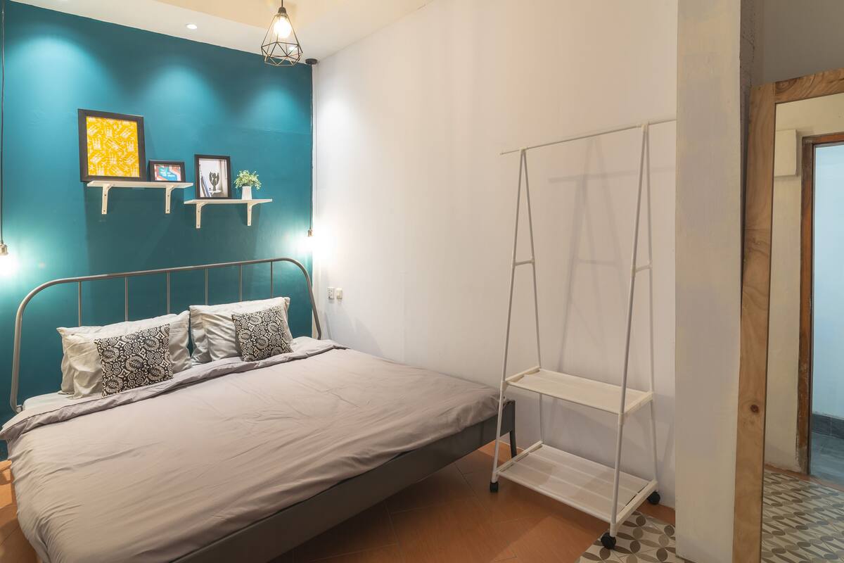 A bedroom with a bed, a ladder, and shelves against a teal wall.