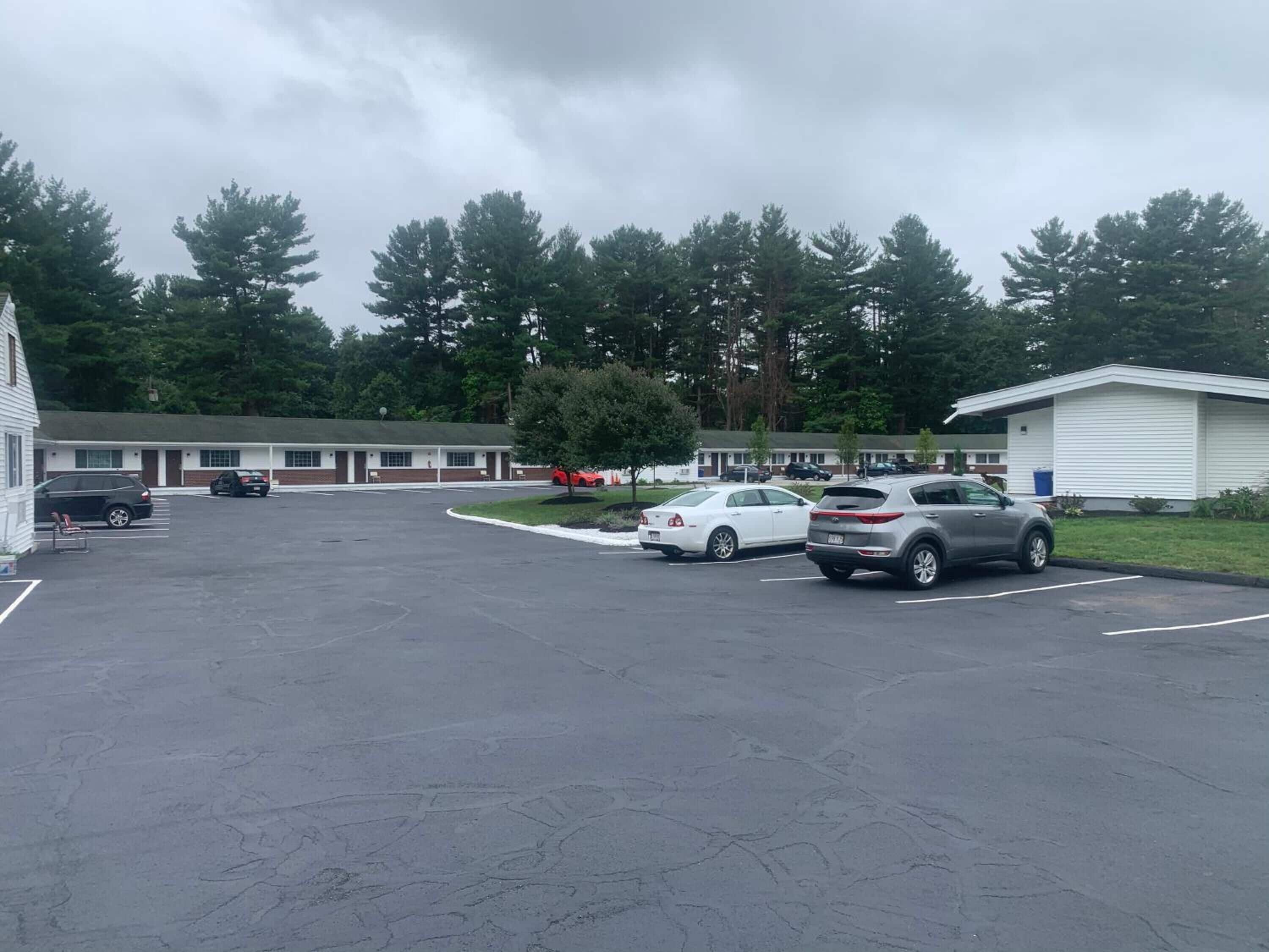 Ein Motel mit Parkplatz, mehreren Autos und einem großen Baum im Hintergrund.
