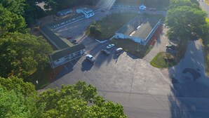 An aerial view of a parking lot with several buildings, including a large white structure with a flat roof and a smaller building with a sloped roof. - Howard Johnson by Wyndham Acton (Acton)