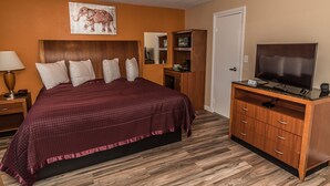 A bedroom with a large bed, wooden headboard, a television on a wooden cabinet, and a mirror above the cabinet. - Howard Johnson by Wyndham Acton (Acton)