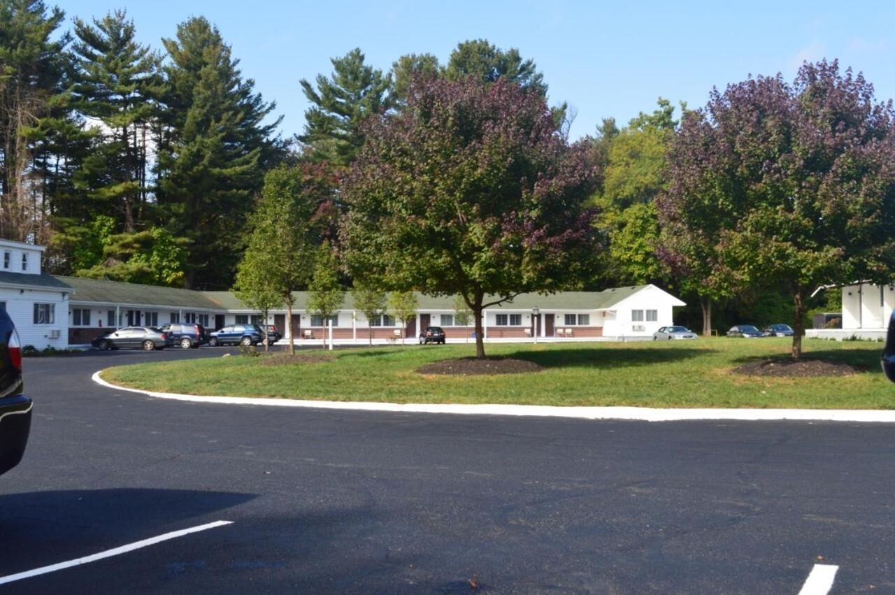 Ein Motel mit mehreren Zimmern, einem Parkplatz und umliegenden Bäumen.