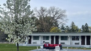 A white single-story house with a red couch and a fire pit in the front yard. - Howard Johnson by Wyndham Acton (Acton)
