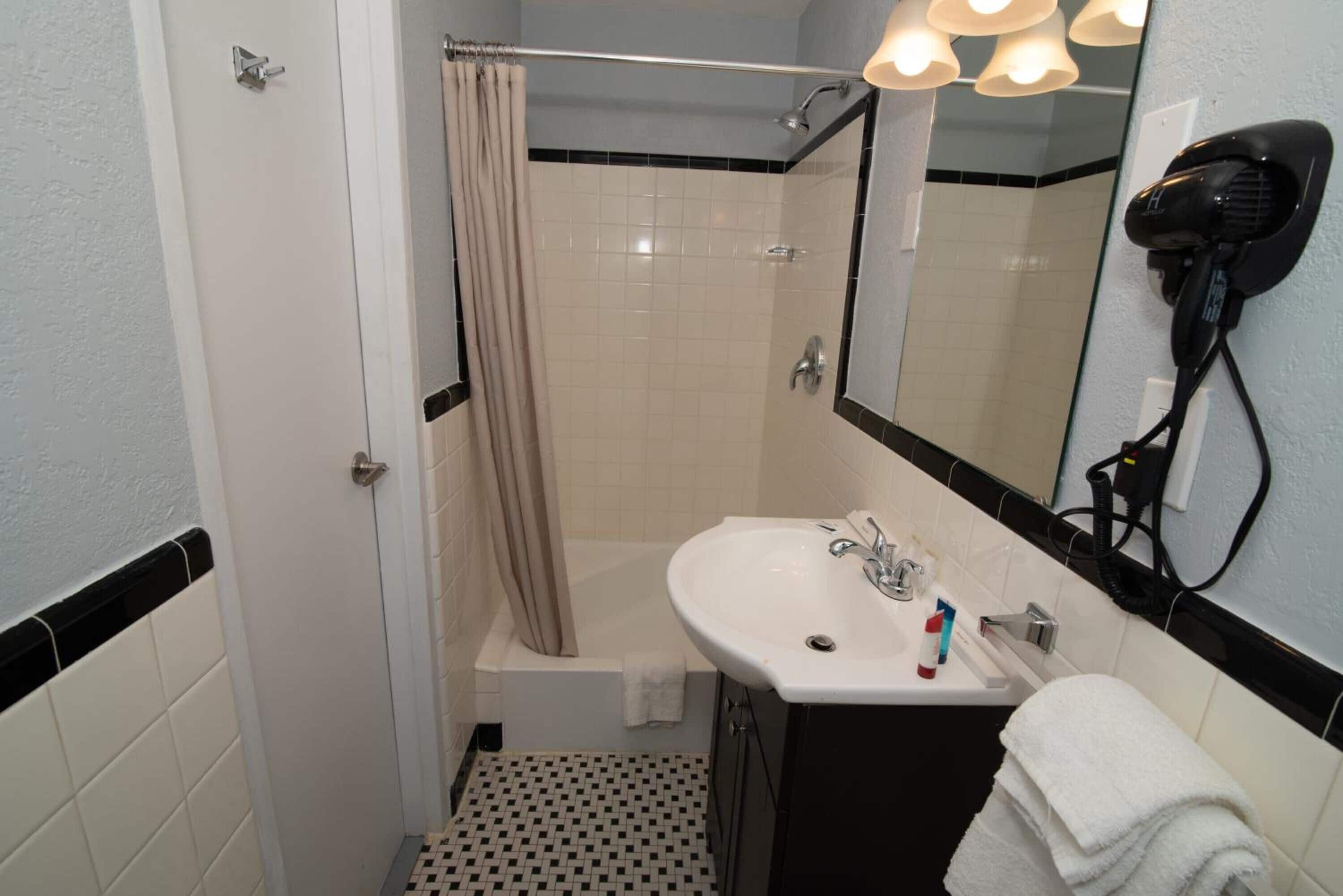 A bathroom with a bathtub, a sink, a mirror, and a hairdryer on the wall.