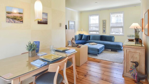A modern living room with a glass dining table, blue sofa, and wooden flooring. - Gorgeous Patio and Deck w/ Central AC! (Provincetown)