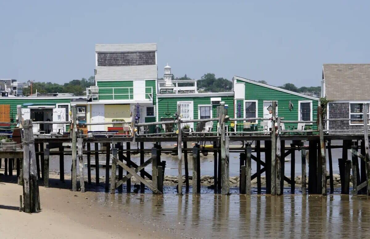 A pier with wooden posts and a green building with a white roof.