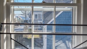 A window with a view of a residential area, including houses and a white picket fence. - Gorgeous Patio and Deck w/ Central AC! (Provincetown)