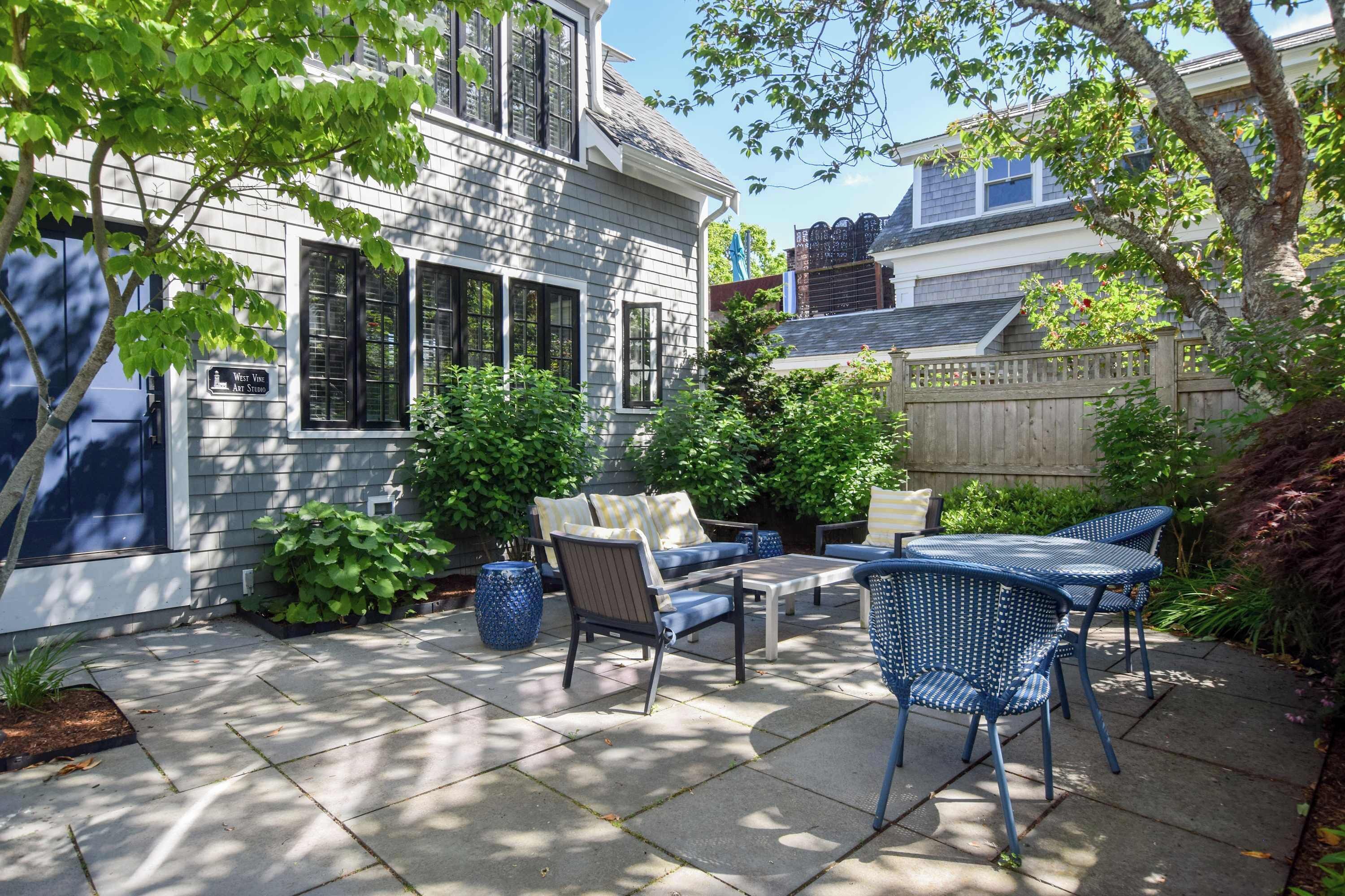 A patio with outdoor furniture, a stone floor, and a house with a sign for 'West Vine Art Studio'.