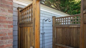 A wooden gate leading to a covered outdoor area with a metal showerhead.