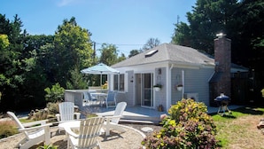 A small house with a patio, outdoor seating, and a barbecue grill.
