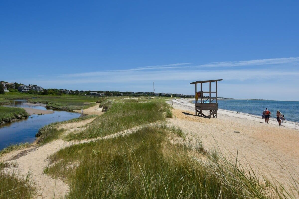 Une plage avec un poste de surveillance pour les sauveteurs, un sentier sablonneux et un petit plan d’eau.