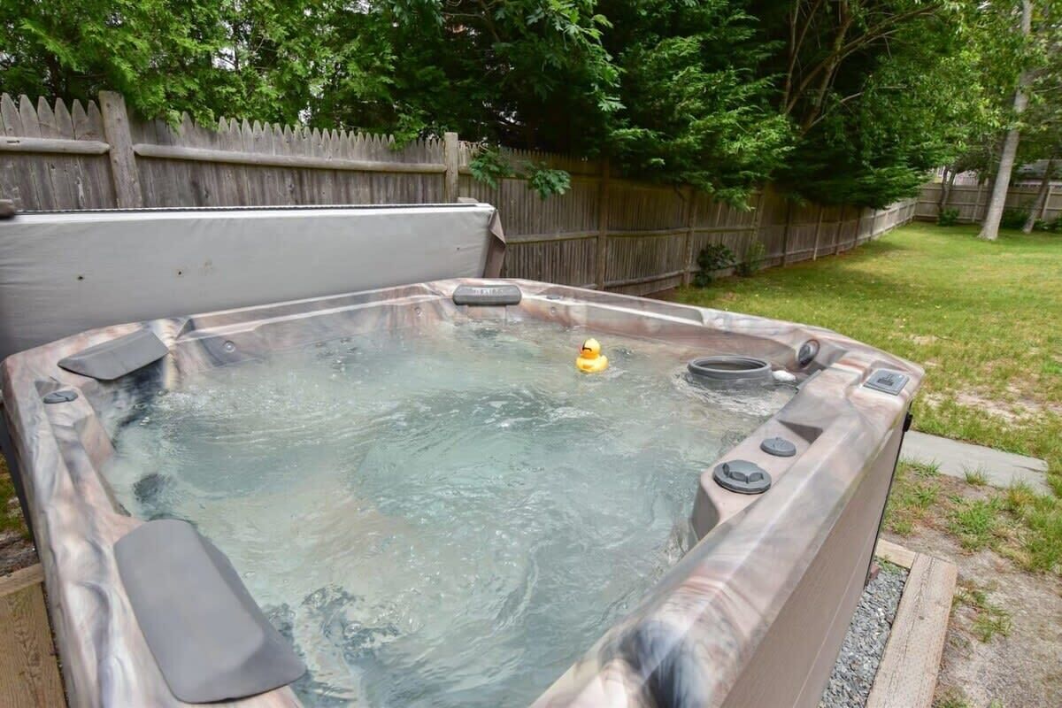 A hot tub in a backyard with a wooden fence and trees in the background.
