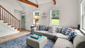 Ein geräumiges Wohnzimmer mit einer Holztreppe, einem grauen Ecksofa und einem blau gemusterten Teppich.
