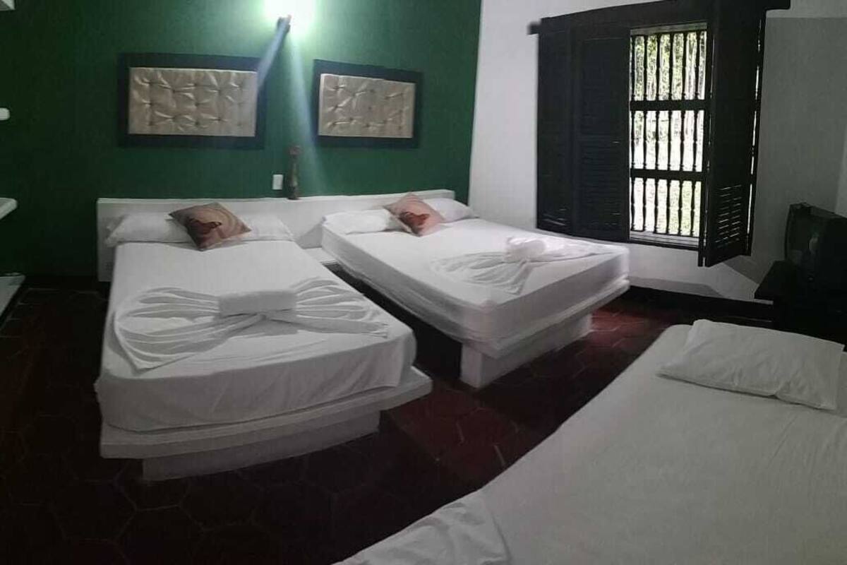 Una habitación con dos camas, una pared verde y una ventana con barrotes.