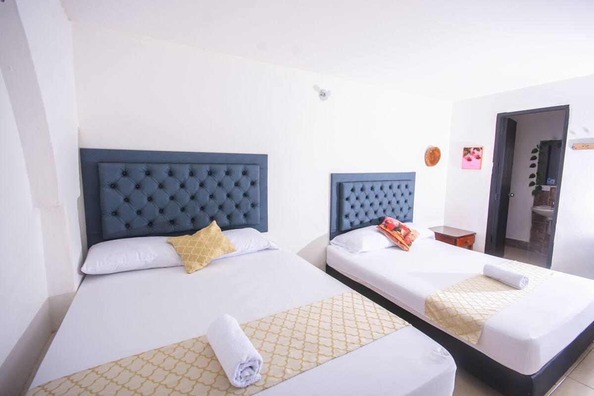 Dos camas individuales con cabeceras azules, ropa de cama blanca y un corredor de cama amarillo estampado.