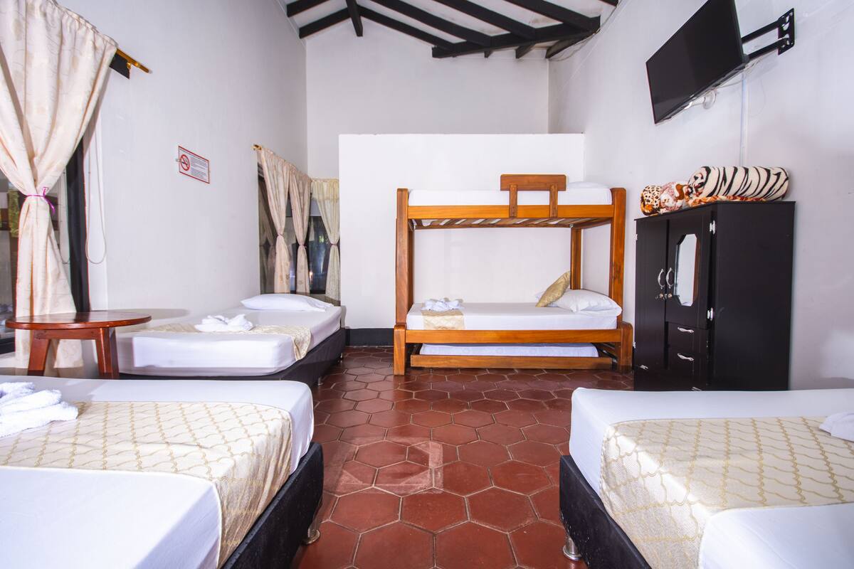 Habitación de hotel con dos camas individuales, una cama nido de madera, una mesita, un armario y un televisor en la pared.