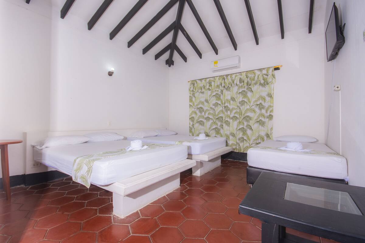 Una habitación con dos camas, una mesita y un televisor en la pared.