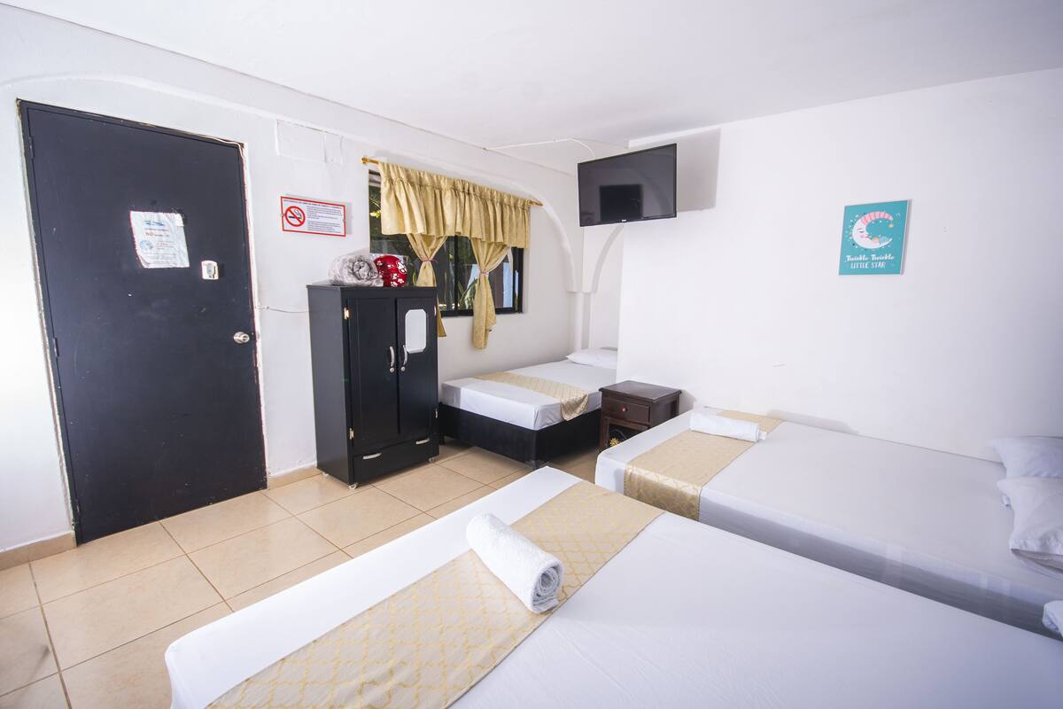 Habitación de hotel con dos camas, un armario, televisión y ventana con cortinas.
