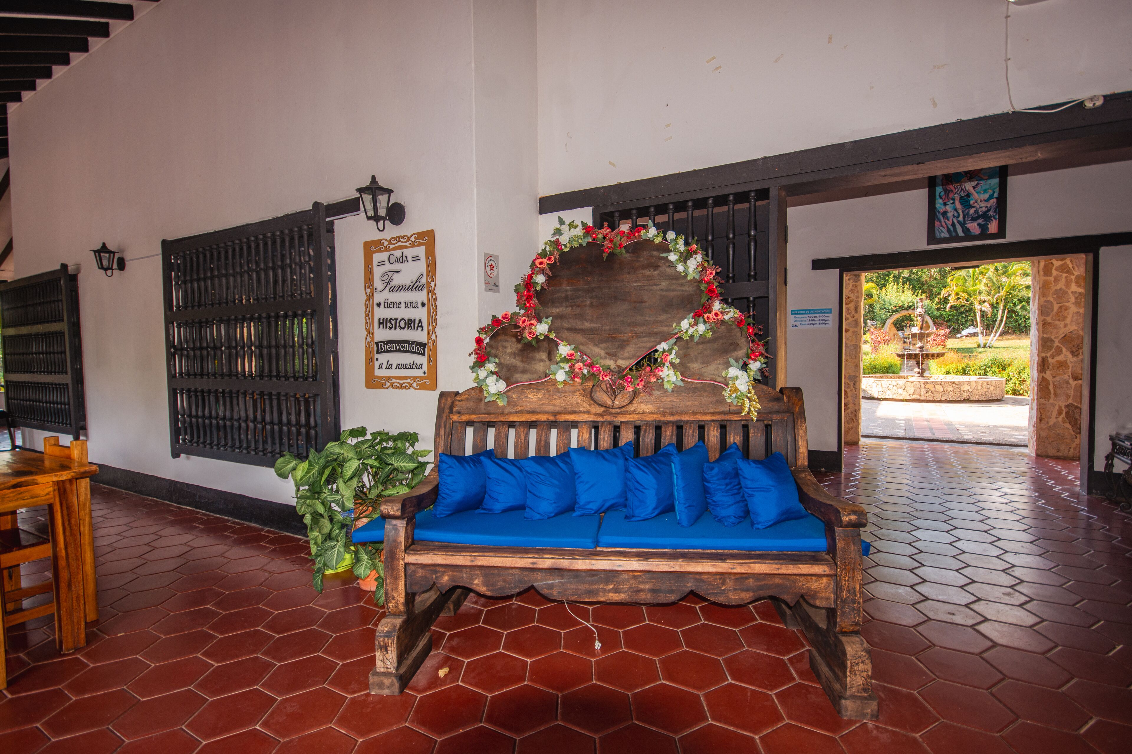 A wooden bench with blue cushions, a decorative heart-shaped frame with flowers, a sign with text, and a tiled floor.