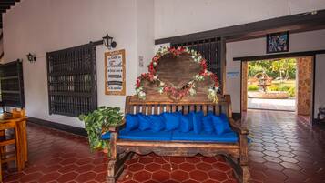 A wooden bench with blue cushions, a decorative heart-shaped frame with flowers, a sign with text, and a tiled floor.